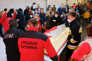 Strażacy wnoszący tort biało czerwony, narodowy, mieszkańcy gminy.