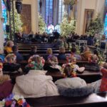Wnętrze kościoła, dzieci siedzace w strojach śląskich na łąwkach w kosciele, w oddali grająca orkiestra