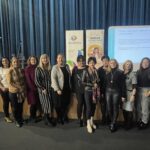 11 kobiet stojących w sali konferencyjnej przed sceną